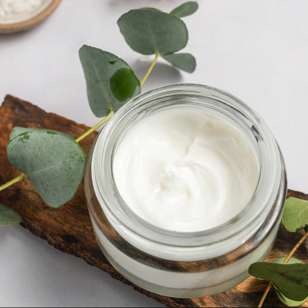 Jar of CBD Emu Oil cream on a wooden board with green leaves and dried flowers on a light background