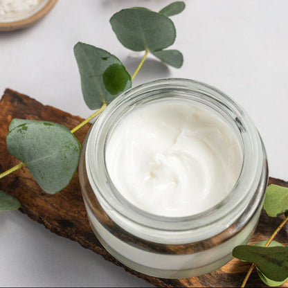 Jar of CBD Emu Oil cream on a wooden board with green leaves and dried flowers on a light background